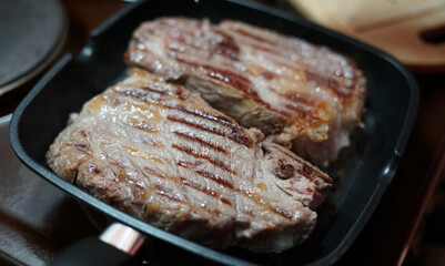 Two large pork steaks are fried in a frying pan at home and adjusted with a fork. On the meat, you can see the stripes from a special frying pan.