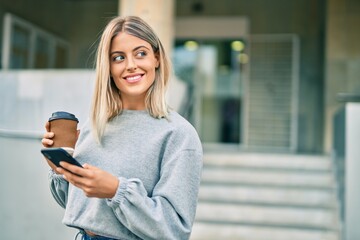 Young blonde girl using smartphone and drinking coffee at the city