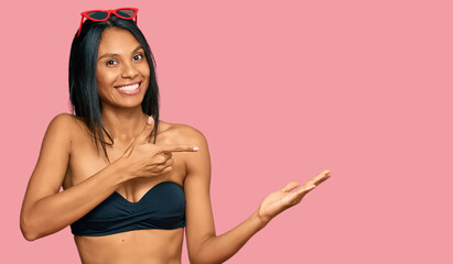 Young african american woman wearing bikini amazed and smiling to the camera while presenting with hand and pointing with finger.