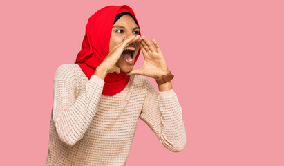 Young african american woman wearing traditional islamic hijab scarf shouting angry out loud with hands over mouth