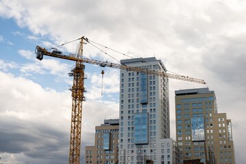 a tower crane is building a monolithic building with office premises in a respectable business-class area against the backdrop of skyscrapers of business centers in a large metropolis