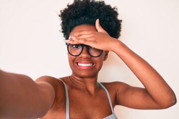 Fototapeta na wymiar Young african american woman wearing casual clothes and glasses making selfie by the camera stressed and frustrated with hand on head, surprised and angry face