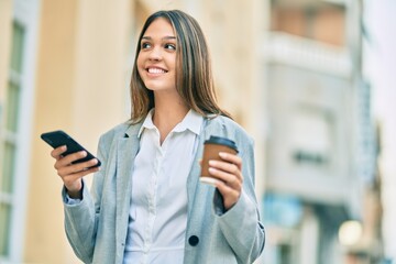 Young latin businesswoman using smartphone and drinking coffee at the city.