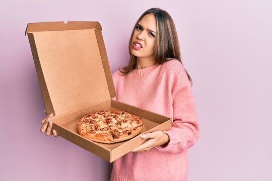 Young brunette woman holding italian pizza clueless and confused expression. doubt concept.