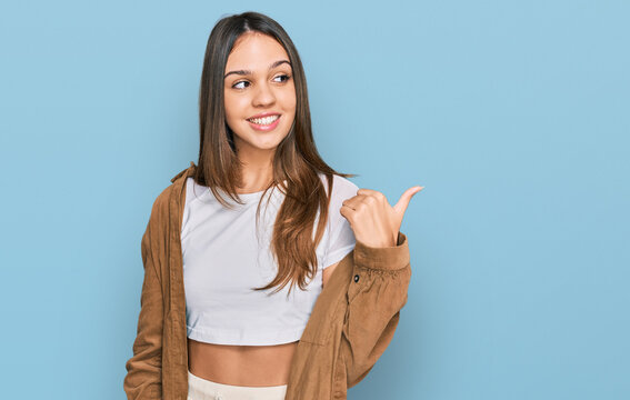 Young brunette woman wearing casual clothes smiling with happy face looking and pointing to the side with thumb up.