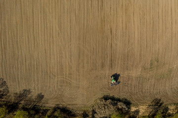 Obraz premium Aerial view large tractor cultivating a dry field. Top down aerial view tractor cultivating ground and seeding a dry field. Aerial tractor cuts furrows in farm field for sowing