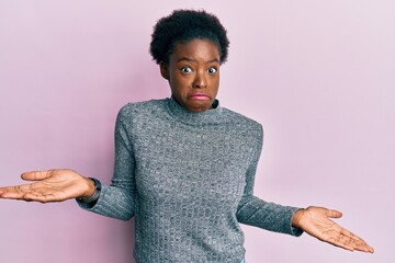 Young african american girl wearing casual clothes clueless and confused expression with arms and...