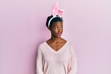 Young african american girl wearing cute easter bunny ears smiling looking to the side and staring...