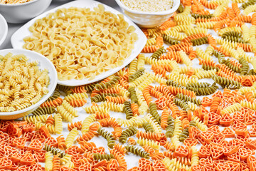 Colorful fusilli and bowls of raw pastas on white background