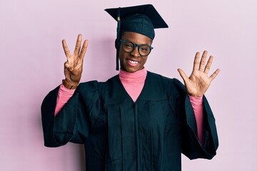 Young african american girl wearing graduation cap and ceremony robe showing and pointing up with fingers number eight while smiling confident and happy.