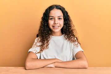 Teenager hispanic girl wearing casual clothes sitting on the table with a happy and cool smile on face. lucky person.