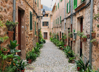 Picturesque Narrow Alley With Cozy Cottages And Green Pot Plants In Valldemossa On Balearic Island Mallorca On An Overcast Winter Day