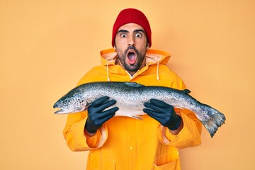 Handsome hispanic man with beard wearing fisherman equipment afraid and shocked with surprise and amazed expression, fear and excited face.