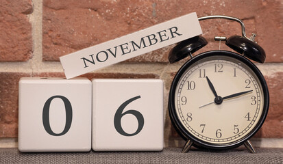Important date, November 6, autumn season. Calendar made of wood on a background of a brick wall. Retro alarm clock as a time management concept.