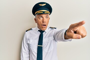 Handsome middle age mature man wearing airplane pilot uniform pointing with finger surprised ahead, open mouth amazed expression, something on the front