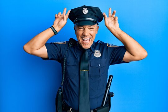 Handsome middle age mature man wearing police uniform posing funny and crazy with fingers on head as bunny ears, smiling cheerful