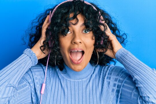 Young hispanic woman listening to music using headphones celebrating crazy and amazed for success with open eyes screaming excited.