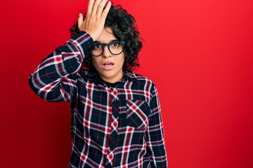 Fototapeta na wymiar Young hispanic woman with curly hair wearing casual clothes and glasses surprised with hand on head for mistake, remember error. forgot, bad memory concept.