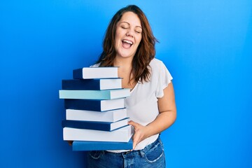 Young caucasian woman holding a pile of books celebrating crazy and amazed for success with open eyes screaming excited.