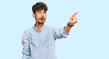 Fototapeta premium Young hispanic man wearing casual clothes pointing with finger surprised ahead, open mouth amazed expression, something on the front