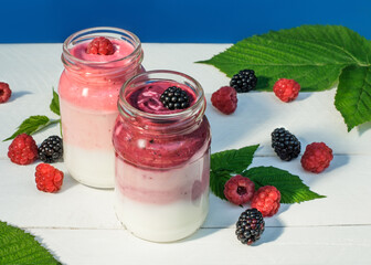 Berry and yogurt smoothies on white table with fresh raspberries and blackberries
