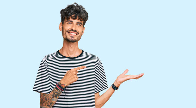 Young hispanic man wearing casual clothes amazed and smiling to the camera while presenting with hand and pointing with finger.