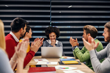 Fototapeta premium Successful mixed race businesswoman sitting in boardroom with her colleagues on meeting. Colleagues clapping for an excellent idea.