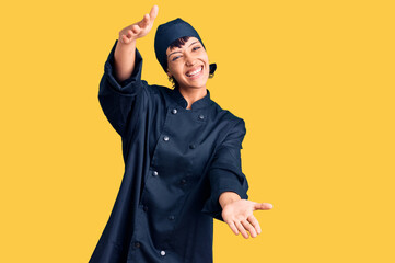 Young brunette woman with short hair wearing professional cook uniform looking at the camera smiling with open arms for hug. cheerful expression embracing happiness.