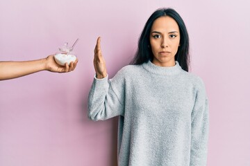 Young hispanic girl rejecting bowl with sugar thinking attitude and sober expression looking self...