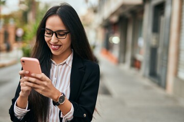 Fototapeta premium Young hispanic businesswoman smiling happy using smartphone at the city.
