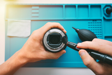 Close up of man hands cleaning camera lens with brush or lens pen cleaner and air blower. Photography equipment care