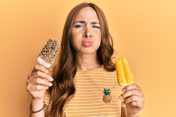 Young brunette woman wearing summer style holding ice cream puffing cheeks with funny face. mouth inflated with air, catching air.