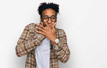 Young african american man with beard wearing casual clothes and glasses shocked covering mouth...