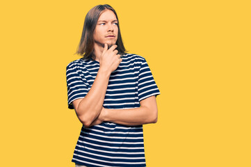 Handsome caucasian man with long hair wearing casual striped t-shirt with hand on chin thinking about question, pensive expression. smiling with thoughtful face. doubt concept.