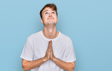 Young caucasian man wearing casual white t shirt begging and praying with hands together with hope...
