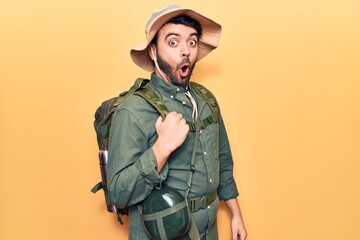Young hispanic man wearing explorer hat and bakcpack scared and amazed with open mouth for...