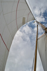 Looking up the mast of a gaff rigged sailing yacht: white sails, wooden mast and gaff, rope shrouds, halyards and sheets, and blue cloudy sunny sky