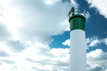 The lighthouse with a green top and white body in Grand Bend, Ontario, Canada towers over the lake against a bright blue, cloudy sky in February, 2021, Lambton Shores, Ontario Canada.