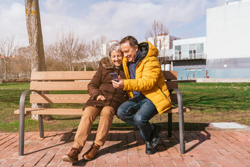 Fototapeta premium Lovely senior couple using a smartphone while sitting on a bench in the park