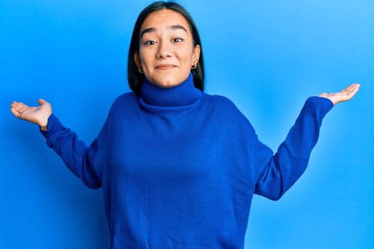 Young asian woman wearing casual winter sweater clueless and confused expression with arms and hands raised. doubt concept.