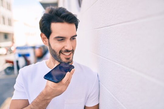Young hispanic man smiling happy sending audio message using smartphone at city.