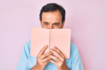 Middle age hispanic man reading book smiling and laughing hard out loud because funny crazy joke.