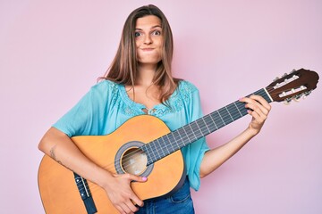 Fototapeta premium Beautiful caucasian woman playing classical guitar puffing cheeks with funny face. mouth inflated with air, catching air.