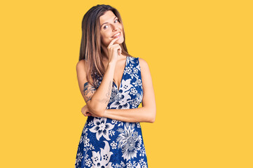 Beautiful caucasian woman wearing summer dress looking confident at the camera with smile with crossed arms and hand raised on chin. thinking positive.