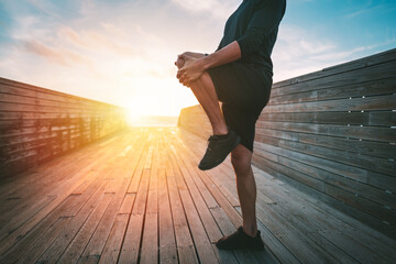 Fototapeta premium Healthy young man stretching legs before workout outdoors at sunset or sunrise. Stretching gluteus maximus muscle. Runner preparing to run.