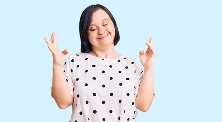 Fototapeta na wymiar Brunette woman with down syndrome wearing casual clothes gesturing finger crossed smiling with hope and eyes closed. luck and superstitious concept.