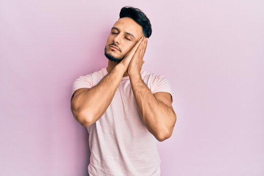 Young arab man wearing casual clothes sleeping tired dreaming and posing with hands together while smiling with closed eyes.