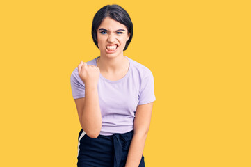 Obraz premium Brunette teenager girl wearing casual clothes angry and mad raising fist frustrated and furious while shouting with anger. rage and aggressive concept.