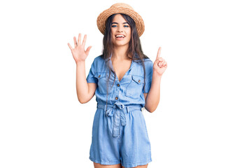 Obraz na płótnie Canvas Brunette teenager girl wearing summer hat showing and pointing up with fingers number six while smiling confident and happy.