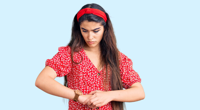 Brunette teenager girl wearing summer dress checking the time on wrist watch, relaxed and confident